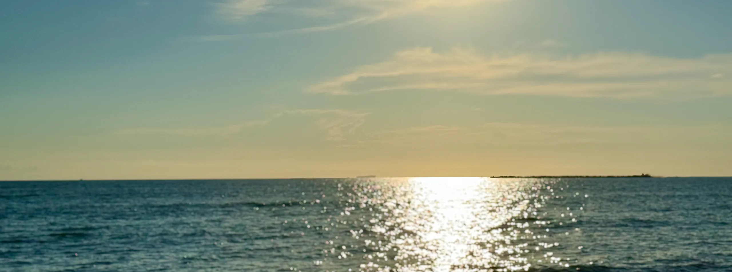 夕方の海。水平線の上に空が広がり、日の光が海面に道をつくっている